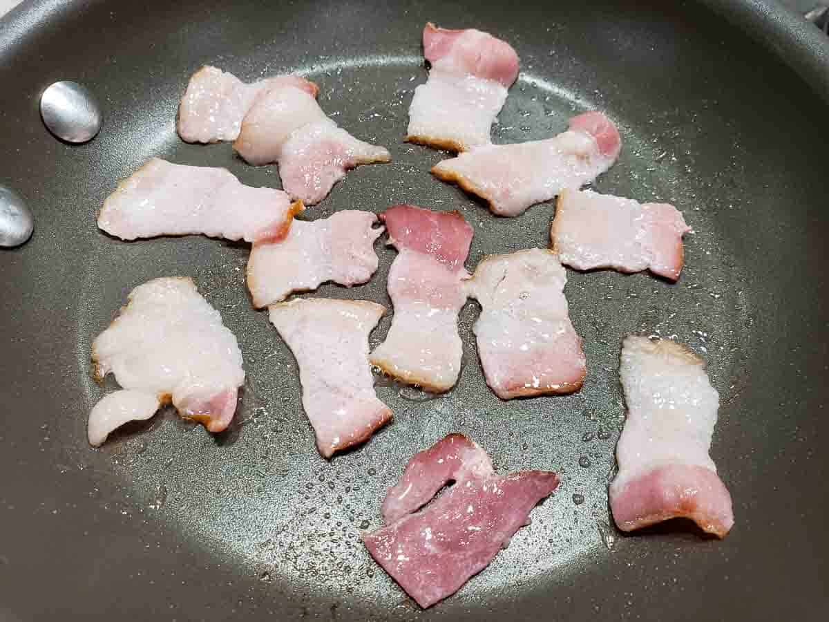 1 inch bacon pieces cooking in a frying pan
