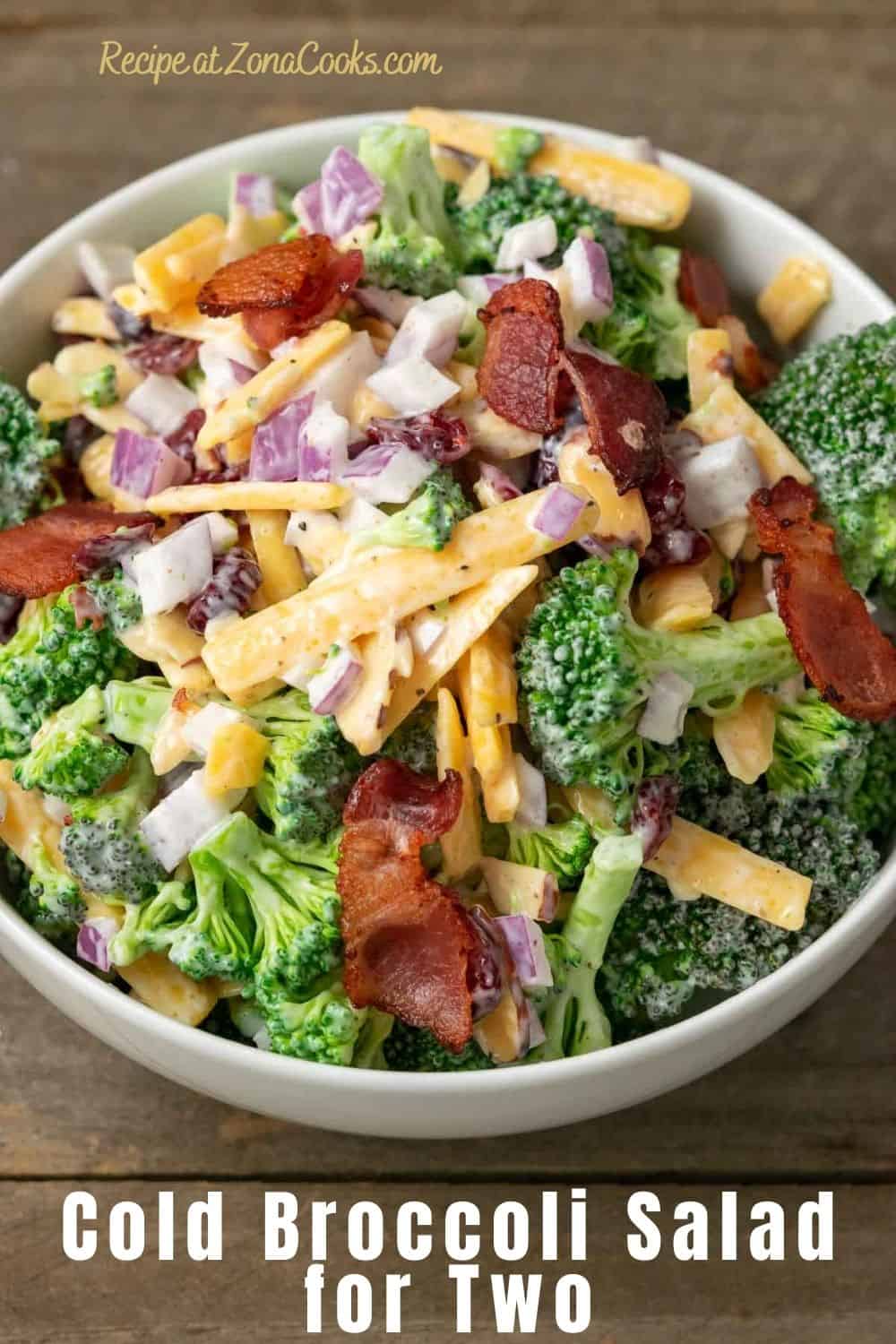 a bowl filled with broccoli, red onion, bacon, cranberries and shredded cheese coated in a white creamy sauce and text reading recipe at zonacooks.com cold broccoli salad for two