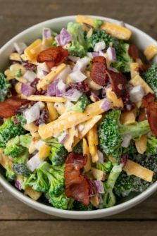 a white bowl filled with broccoli, red onion, bacon, cranberries and shredded cheese coated in a white creamy sauce
