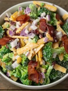 a white bowl filled with broccoli, red onion, bacon, cranberries and shredded cheese coated in a white creamy sauce