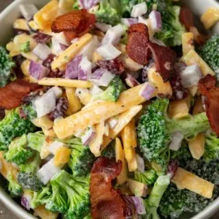 a white bowl filled with broccoli, red onion, bacon, cranberries and shredded cheese coated in a white creamy sauce