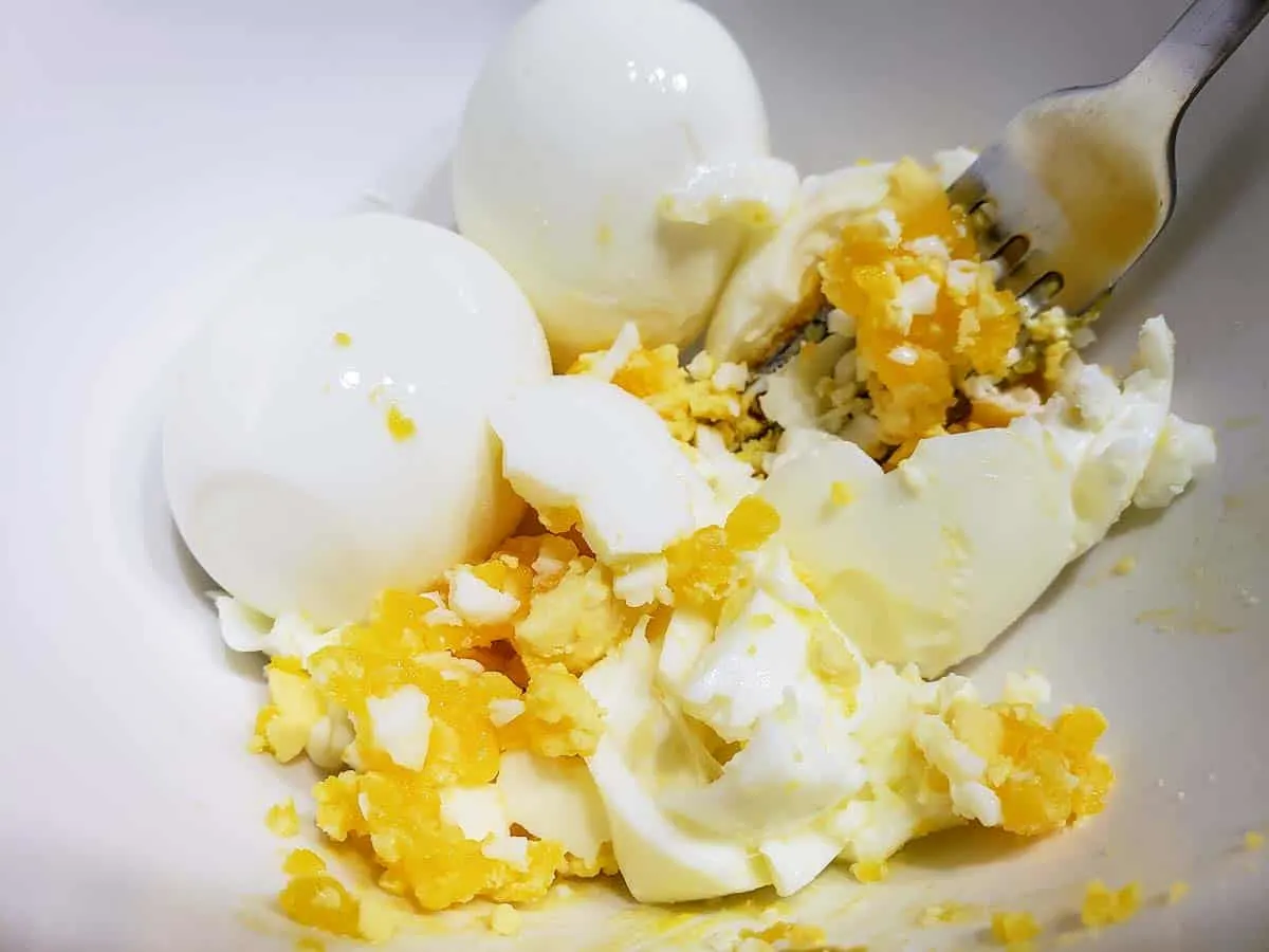 a fork mashing hard boiled eggs in a bowl