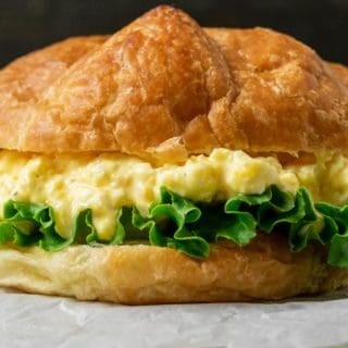 a large croissant filled with lettuce and creamy yellow chopped egg salad mixture on parchment paper