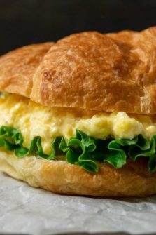 a close up front view of a large croissant filled with lettuce and creamy yellow chopped egg salad mixture