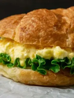 a close up front view of a large croissant filled with lettuce and creamy yellow chopped egg salad mixture