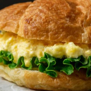 a close up front view of a large croissant filled with lettuce and creamy yellow chopped egg salad mixture