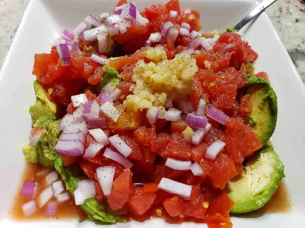 avocado slices topped with tomatoes, red onions, garlic, salt and pepper in a bowl