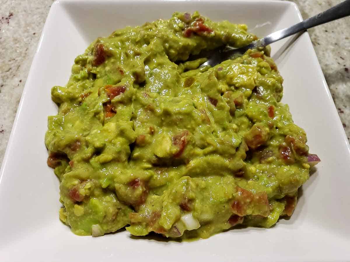 guacamole with canned tomatoes and red onions mixed in a bowl