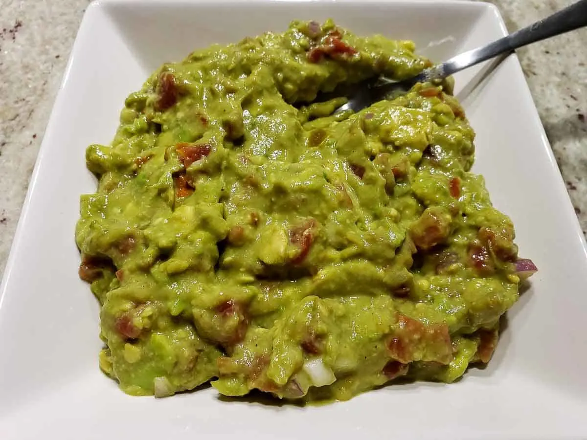 guacamole with canned tomatoes and red onions mixed in a bowl