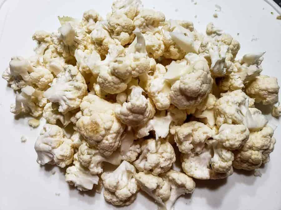 raw cauliflower chopped into florets on a cutting board