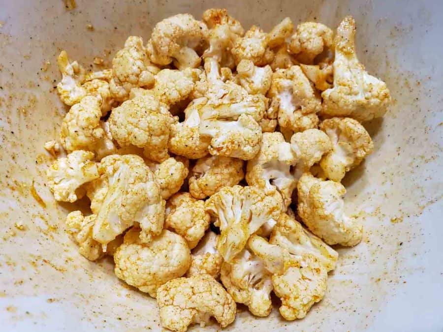 a bowl filled with cauliflower florets coated in oil and seasonings