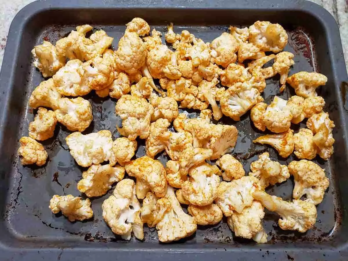 cauliflower florets coated in oil and seasonings spread out on a baking sheet pan