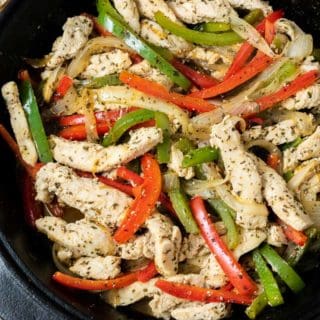 a cast iron skillet filled with sliced green pepper, red pepper, onions, and chicken in homemade fajita seasoning and fire roasted tortillas