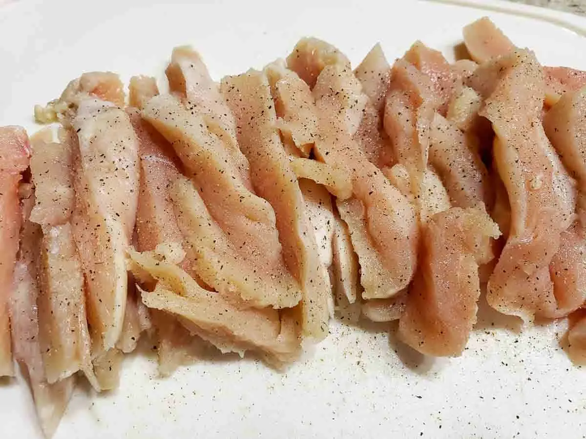 sliced boneless chicken sprinkled with salt and pepper on a cutting board.