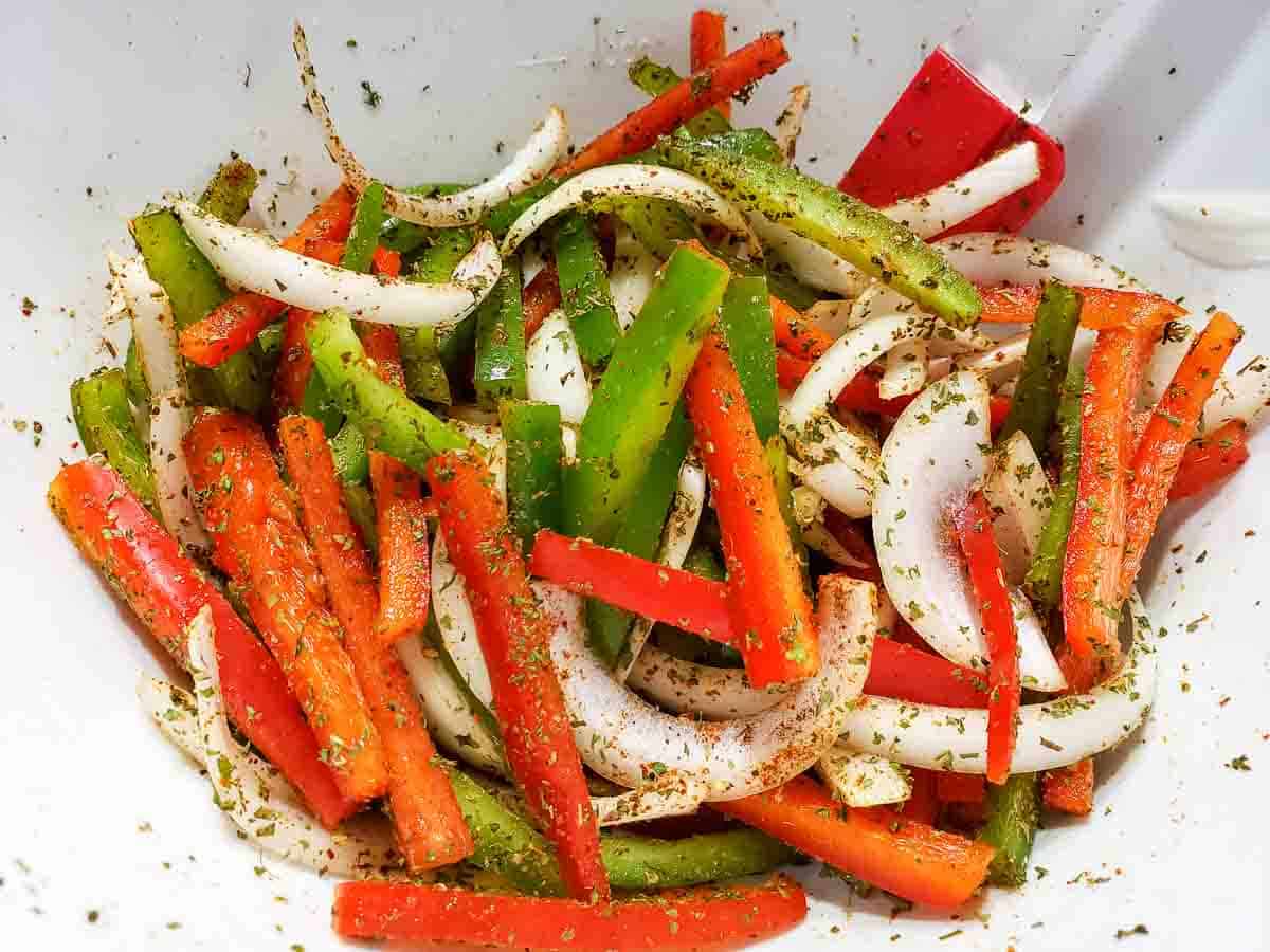 sliced green peppers, red peppers and onions coated in the best fajita seasoning in a bowl.