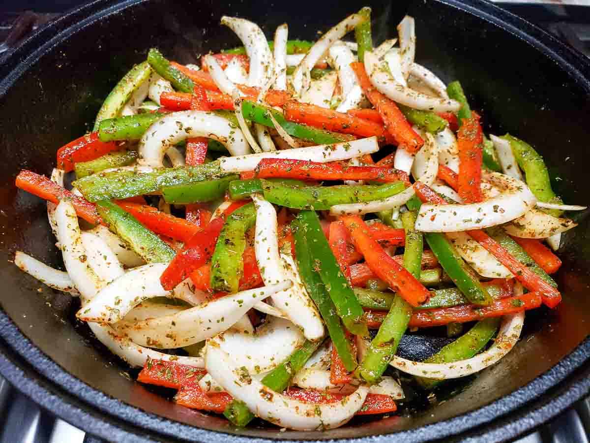 sliced green peppers, red peppers and onions coated in the best fajita seasoning in a cast iron skillet.
