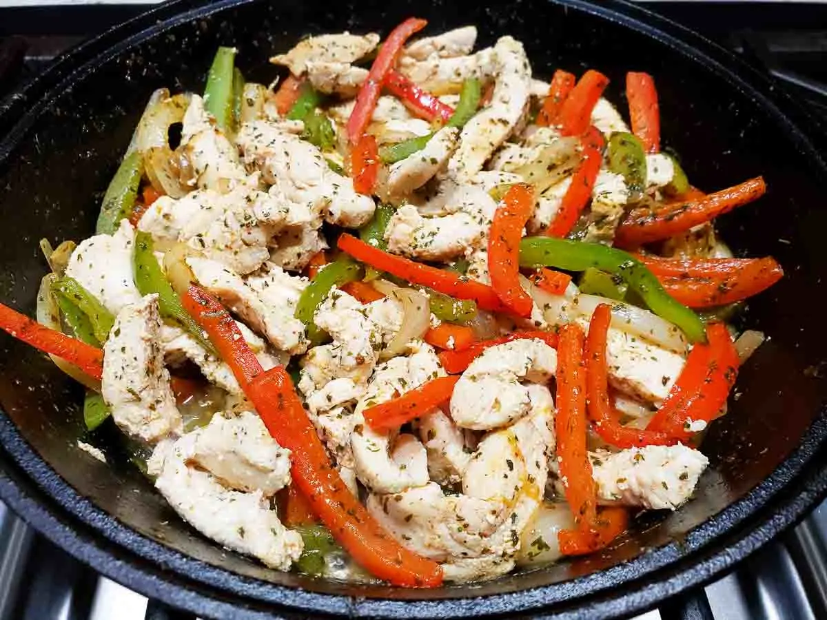 sliced green peppers, red peppers and onions coated in the best fajita seasoning and boneless chicken slices mixed together cooking in a cast iron skillet.