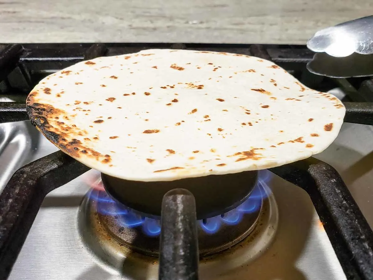 a flour tortilla cooking over an open flame on a gas stove.