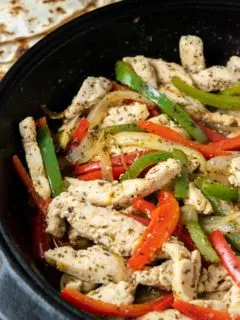 fire roasted tortillas and a cast iron skillet filled with sliced green pepper, red pepper, onions, and chicken in homemade fajita seasoning