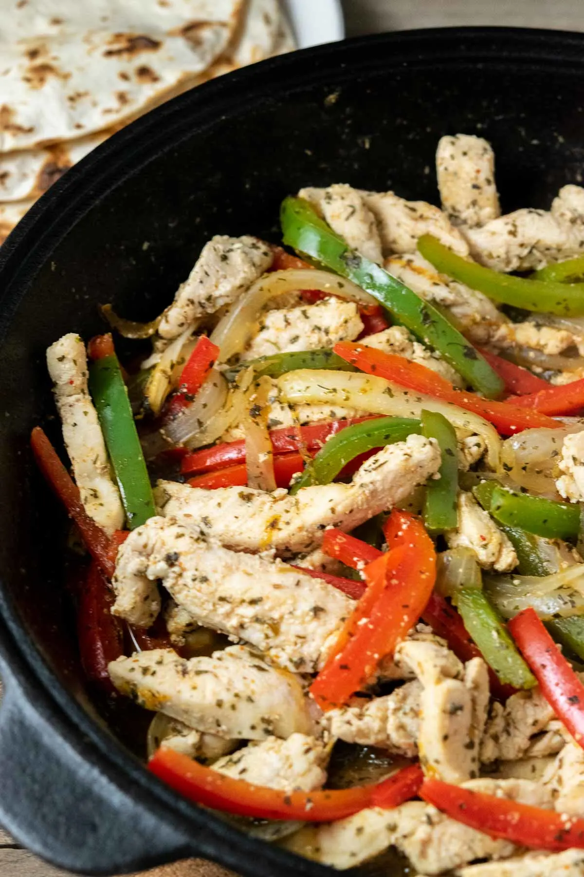 fire roasted tortillas and a cast iron skillet filled with sliced green pepper, red pepper, onions, and chicken in homemade fajita seasoning