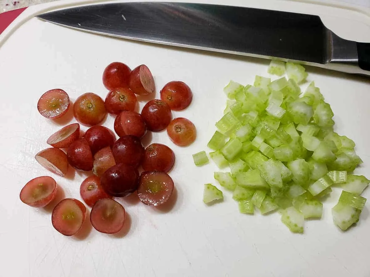 sliced grapes and diced celery on a cutting board with a chefs knife.