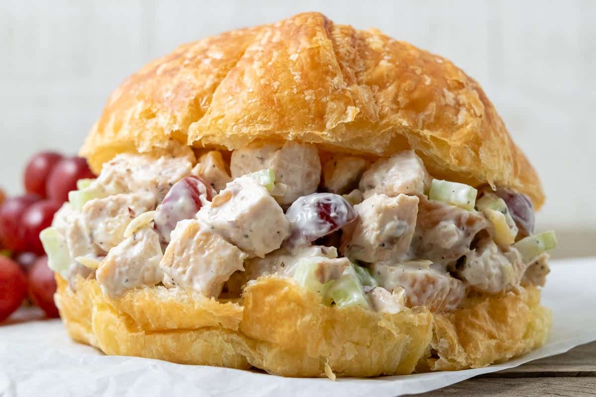 Chicken Salad Croissant with boneless chicken, grapes, almonds, and celery coated in a mayo dressing piled in a large buttery croissant roll.