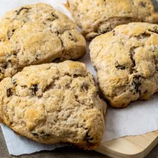 fluffy golden brown scones filled with cinnamon and raisins and topped with coarse sugar and sitting on parchment paper