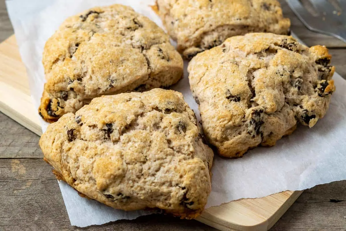 fluffy golden brown scones filled with cinnamon and raisins and topped with coarse sugar and sitting on parchment paper