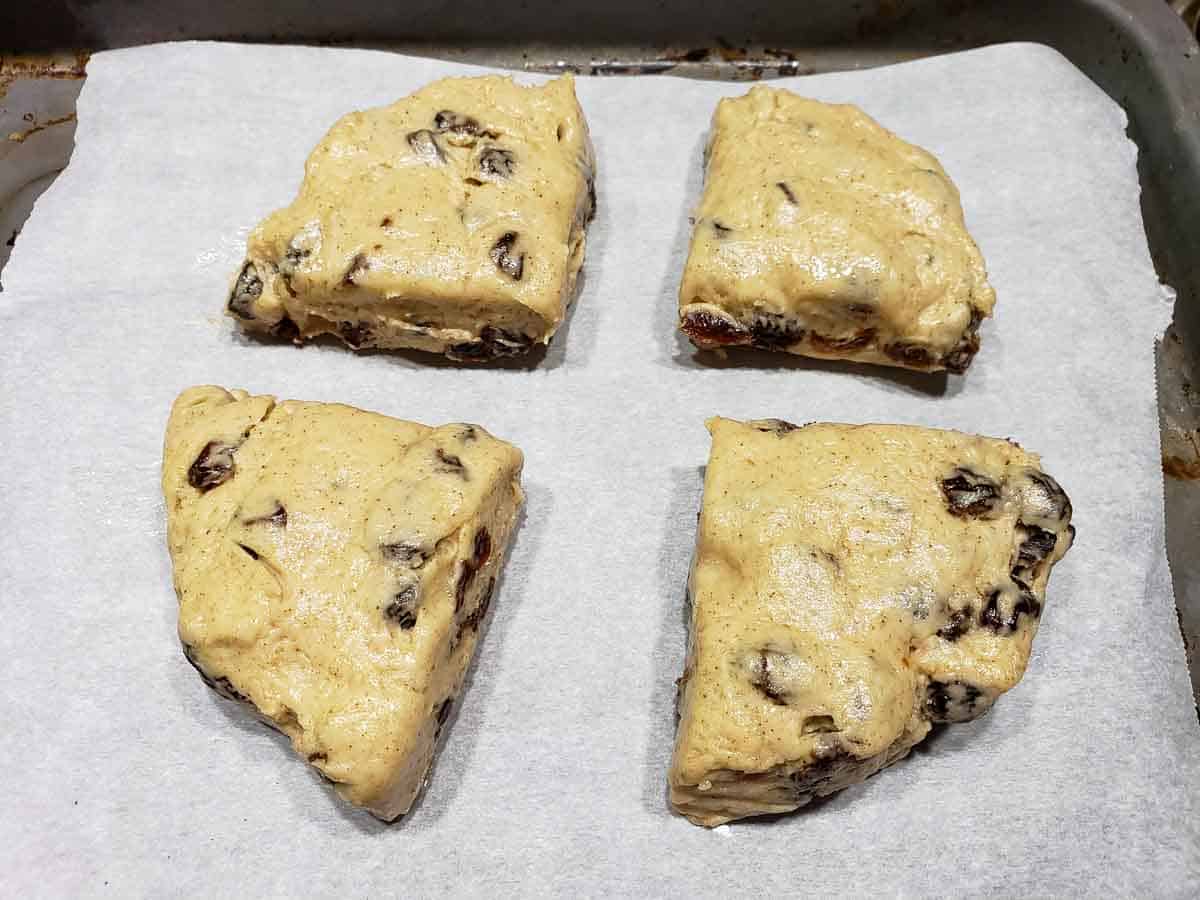 4 unbaked cinnamon raisin scones on a baking sheet