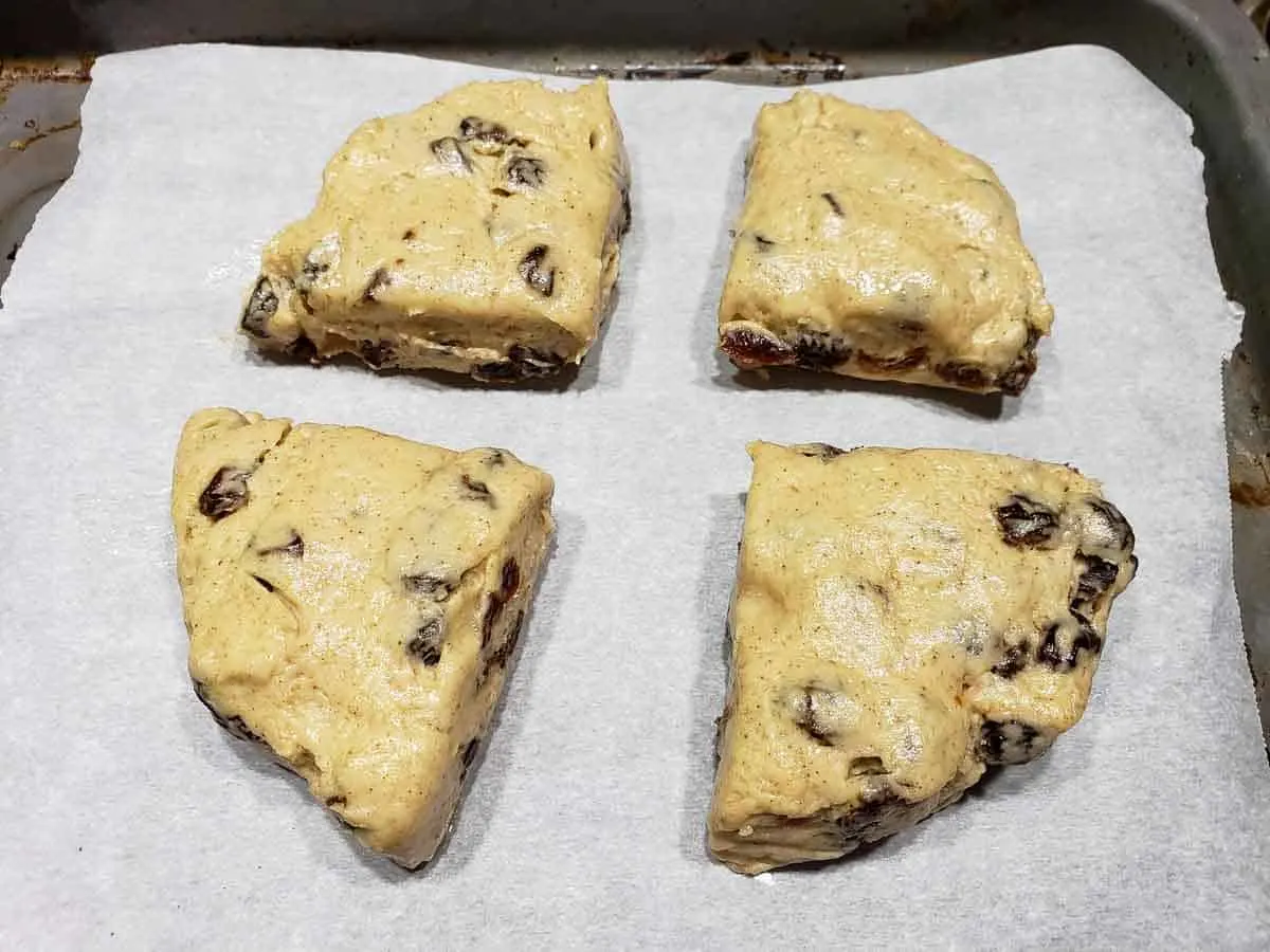 4 unbaked cinnamon raisin scones on a baking sheet