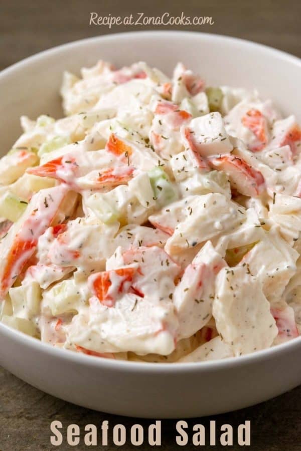 a bowl of seafood salad with chopped imitation crab meat combined with onion and celery in a creamy mayonnaise dressing and text reading recipe at zonacooks.com seafood salad.