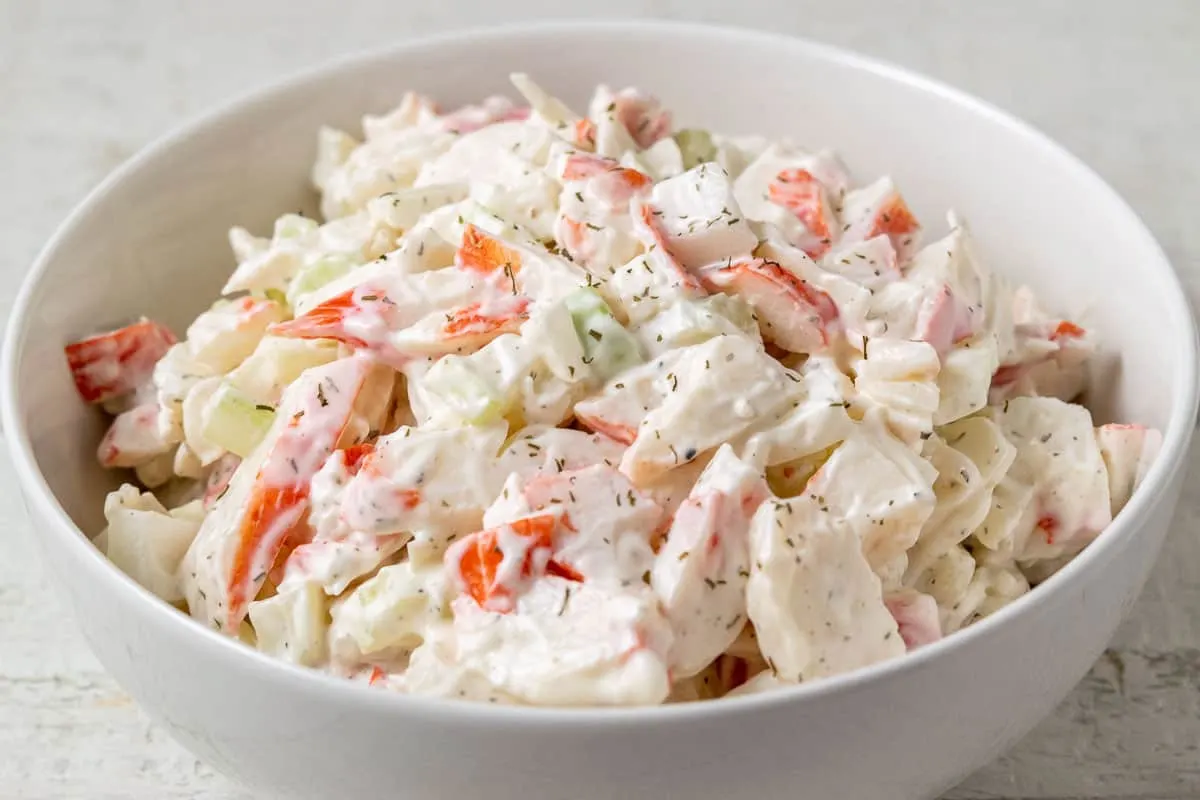 a bowl of cold seafood salad with chopped imitation crab meat combined with onion and celery in a creamy mayonnaise dressing.