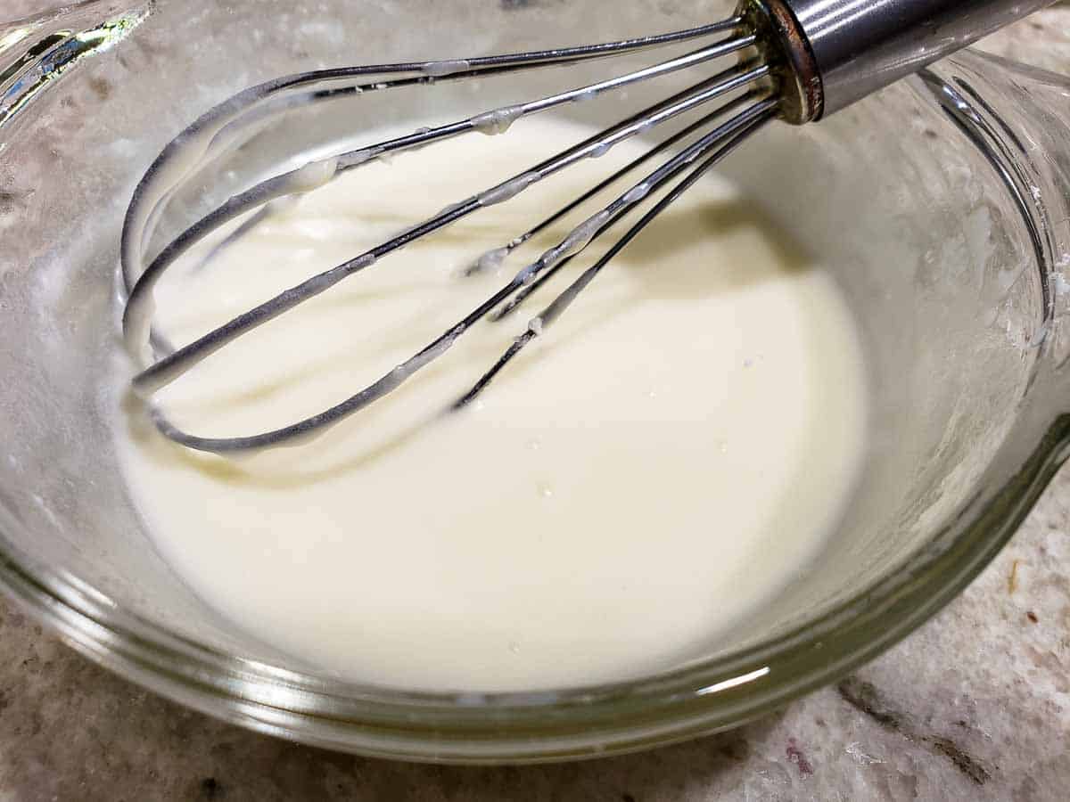 white creamy powdered sugar glaze mixed in a bowl with a whisk