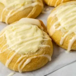 4 golden brown crescent dough circles topped with a cream cheese filling in the center and a white creamy glaze drizzle