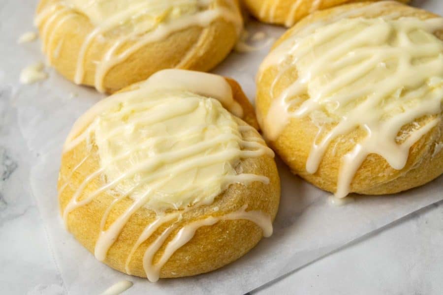 4 golden brown crescent dough circles topped with a cream cheese filling in the center and a white creamy glaze drizzle