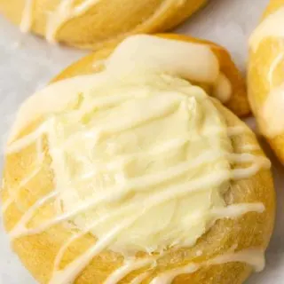 a close up of golden brown crescent dough circles topped with a cream cheese filling in the center and a white creamy glaze drizzle