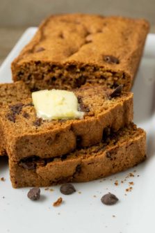 a loaf of easy chocolate chip zucchini bread with 3 slices laying down topped with butter.