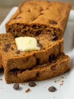 a loaf of easy chocolate chip zucchini bread with 3 slices laying down topped with butter.
