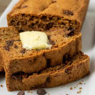 a loaf of easy chocolate chip zucchini bread with 3 slices laying down topped with butter.