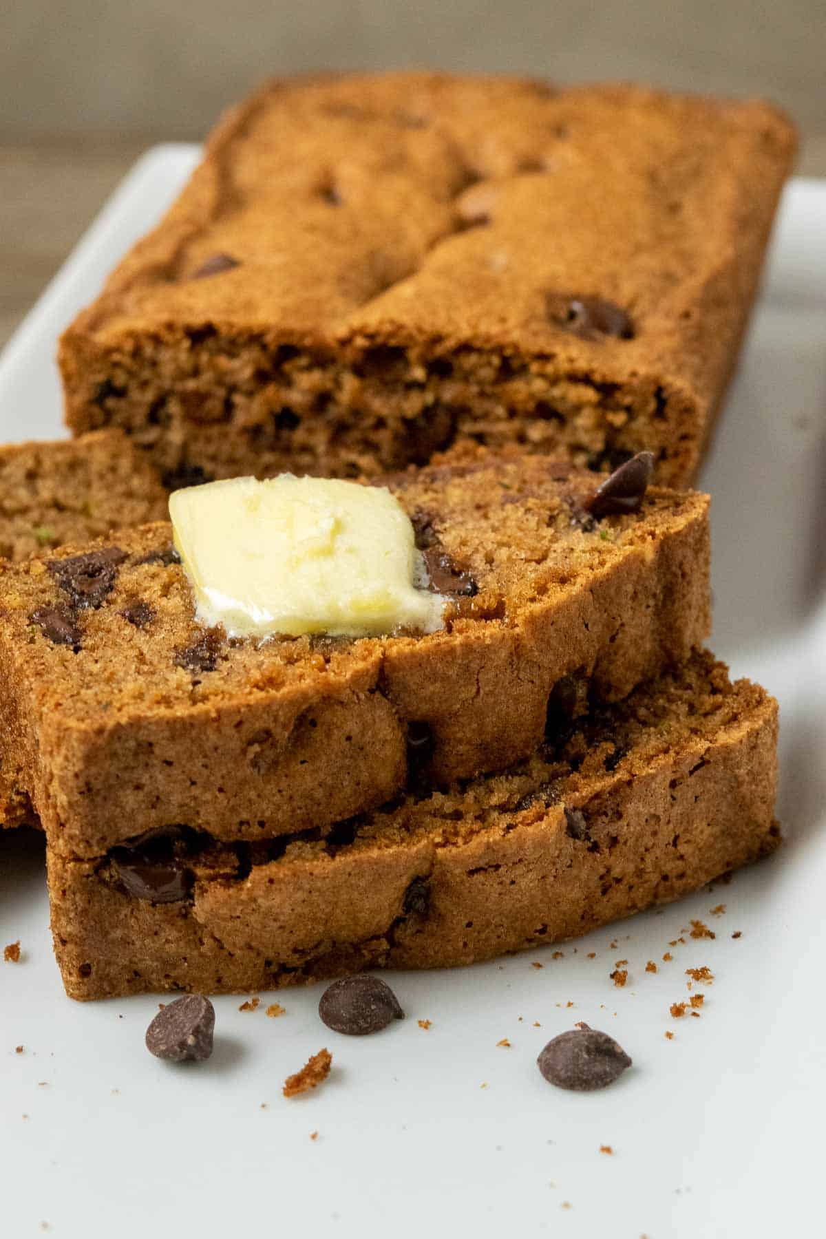a loaf of easy chocolate chip zucchini bread with 3 slices laying down topped with butter.