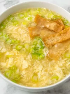 a bowl of egg drop soup topped with crispy wonton croutons.