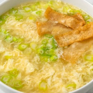 a bowl of egg drop soup with green onions and crispy wonton croutons.