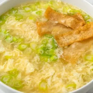 a bowl of egg drop soup with green onions and crispy wonton croutons.