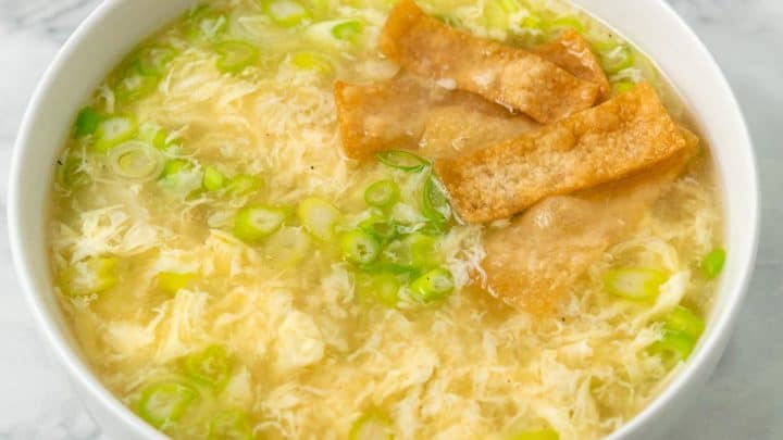a bowl of egg drop soup with green onions and crispy wonton croutons.