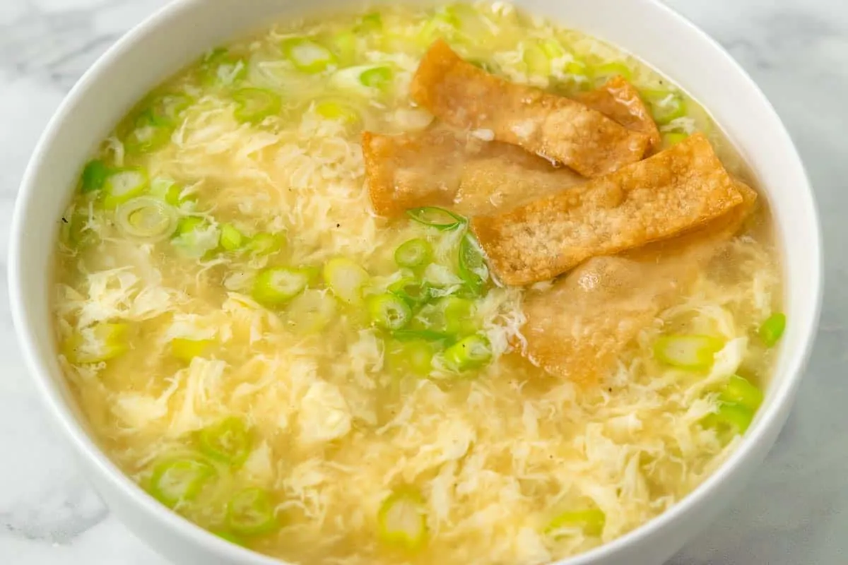 a bowl of egg drop soup with green onions and crispy wonton croutons.