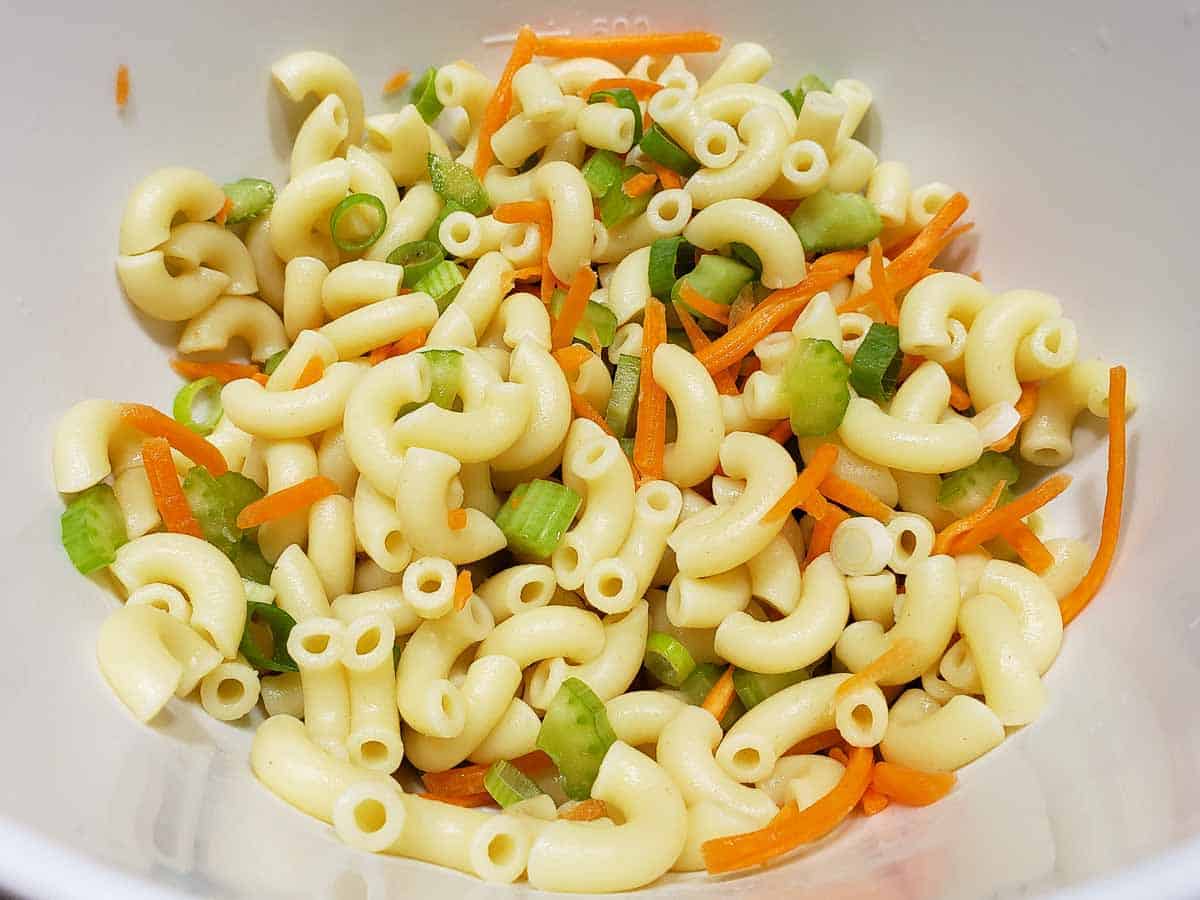 a bowl filled with elbow noodles, carrots, celery, and green onions.