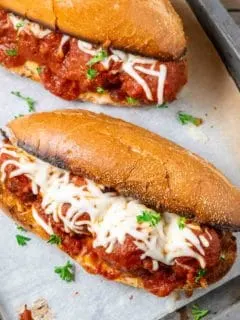 two homemade meatball subs on a baking sheet.