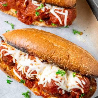 two homemade meatball subs on a baking sheet.