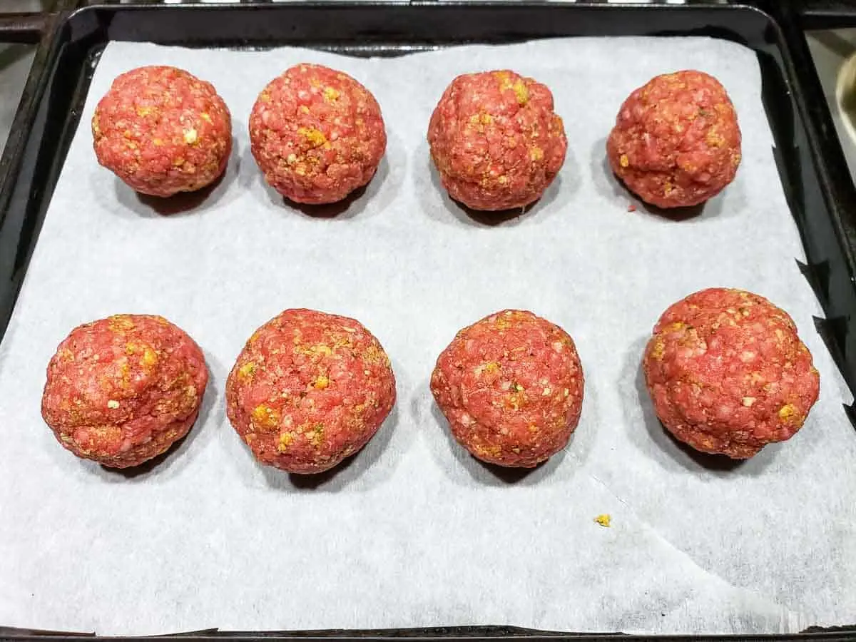 8 uncooked meatballs on a baking sheet.