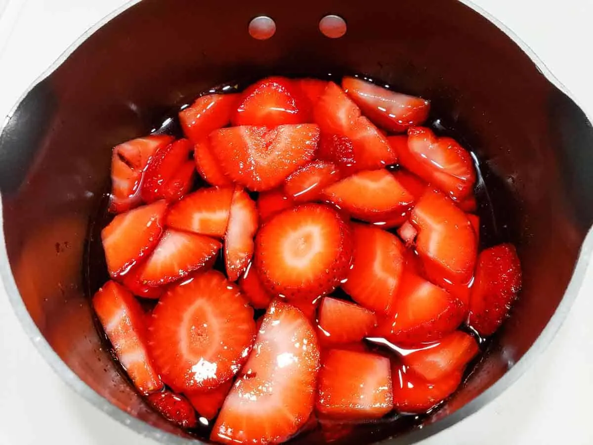 sliced strawberries stirred into red strawberry jello in a sauce pan.